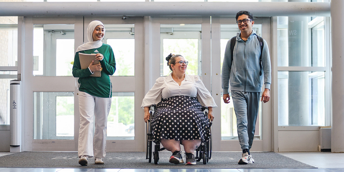 Two people walk and talk with a person in a wheelchair