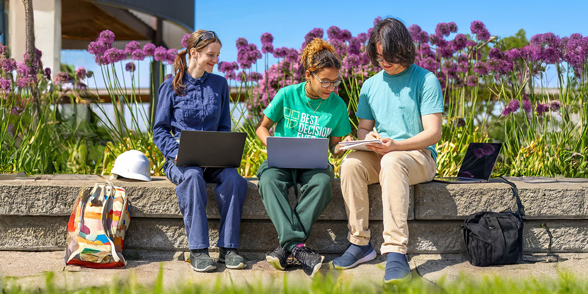 Three students sit outdoors on campus