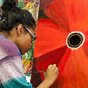woman painting an orange flower on an artboard
