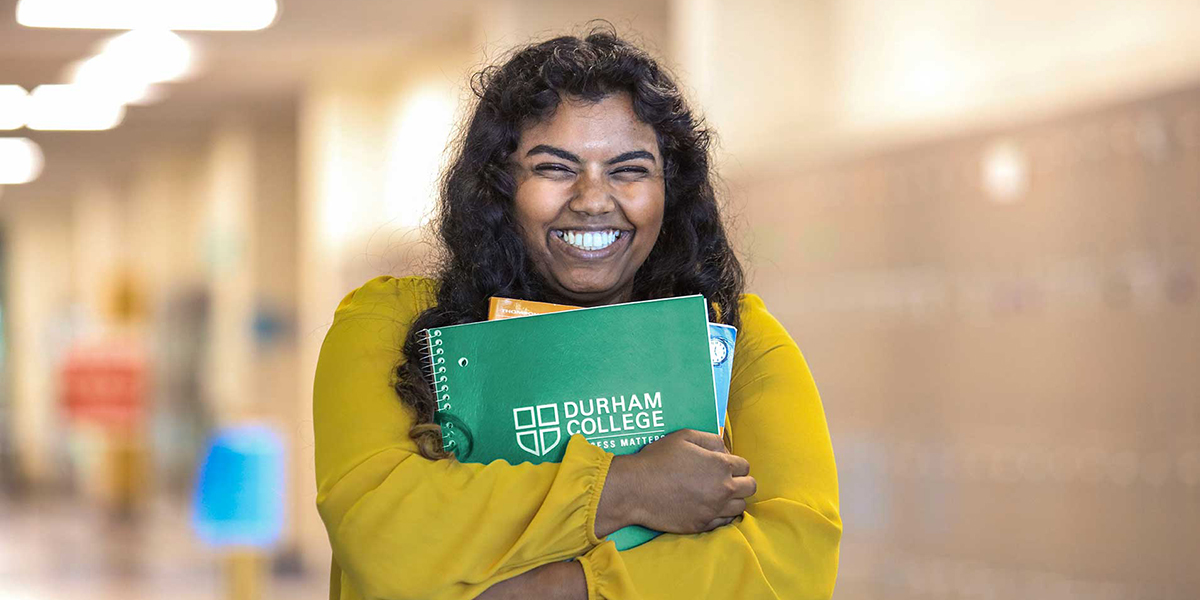 A smiling student clutches her Durham College-branded notebook.