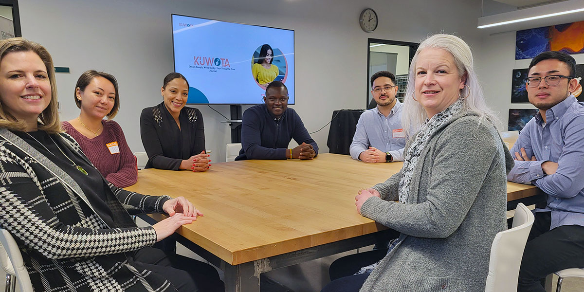 Seven people, including Kinen Ocitti, professor Teresa Avvampato, therapist Kelly Patterson and four DC students sit at a wooden table and smile.