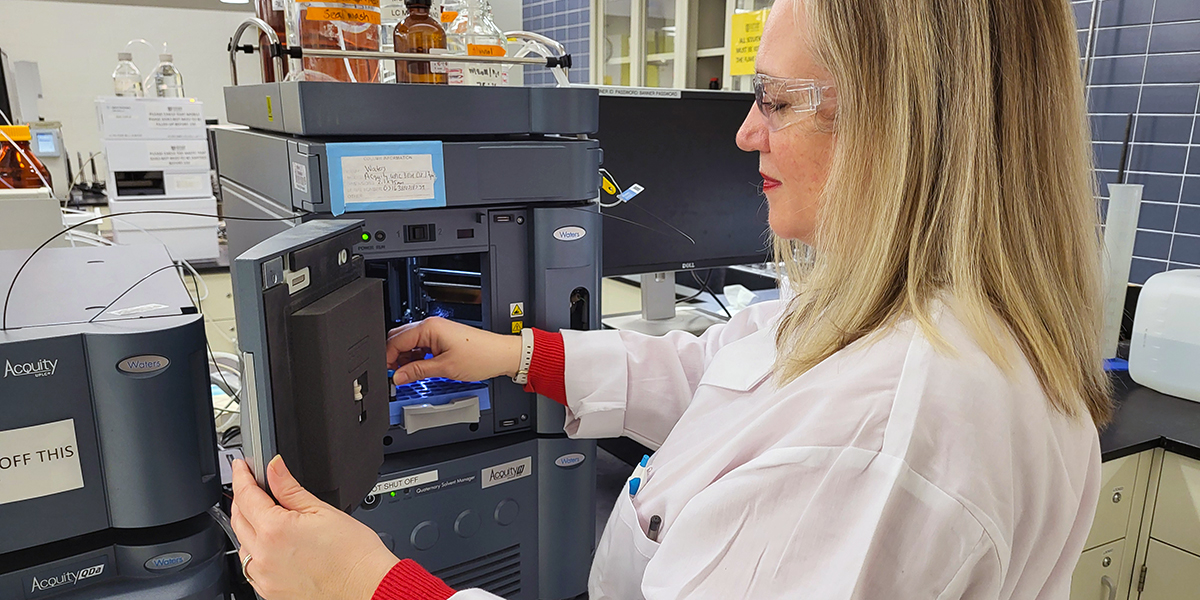 Christine Hand wears a white lab coat and works with scientific equipment.