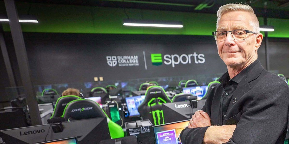 Michael Cameron stands in the Esports Gaming Arena, facing the camera with his arms crossed.