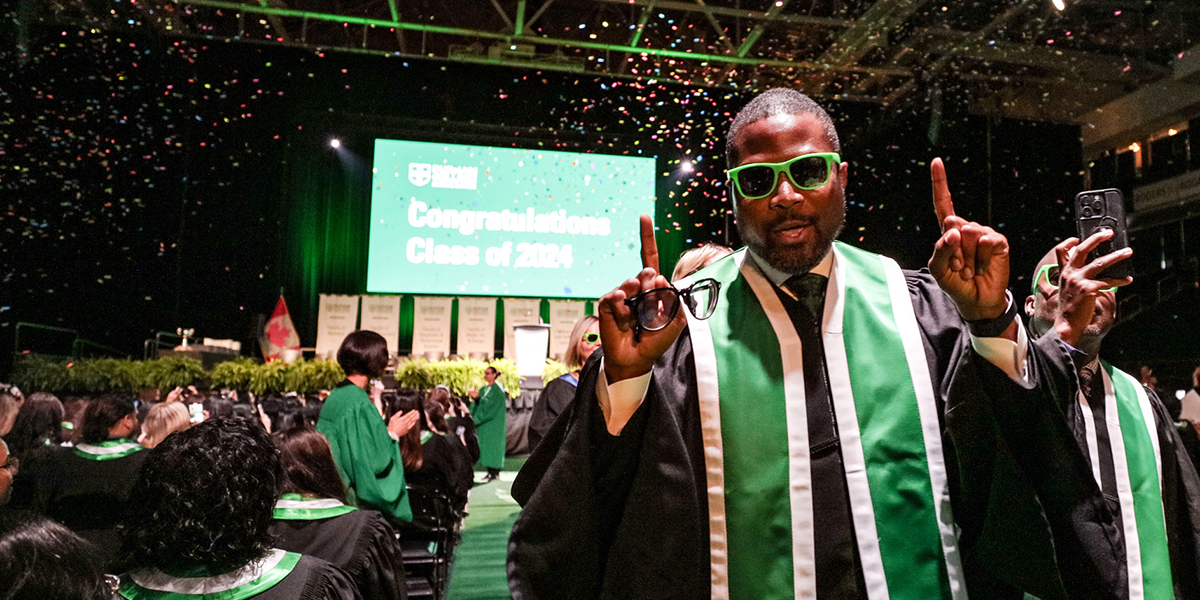 A young man wearing sunglasses points as he celebrates his convocation.