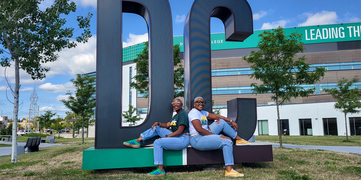 Ashley and Megan Bent sit back to back in front of the DC sign.