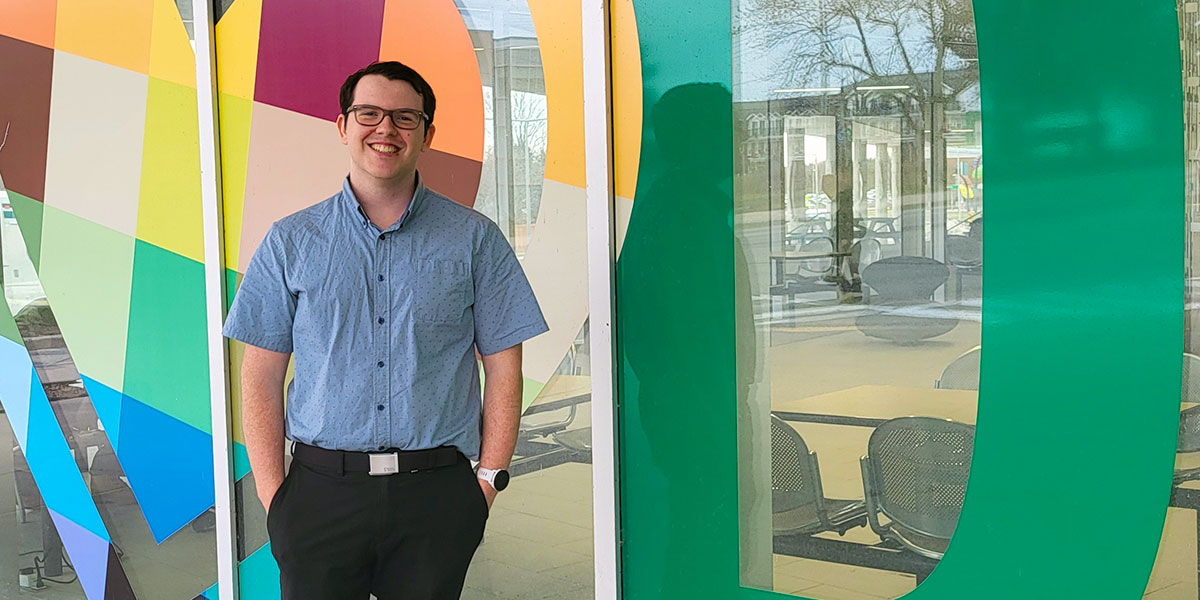 Maxwell stands with hands in his pockets in front of a colorful glass wall.