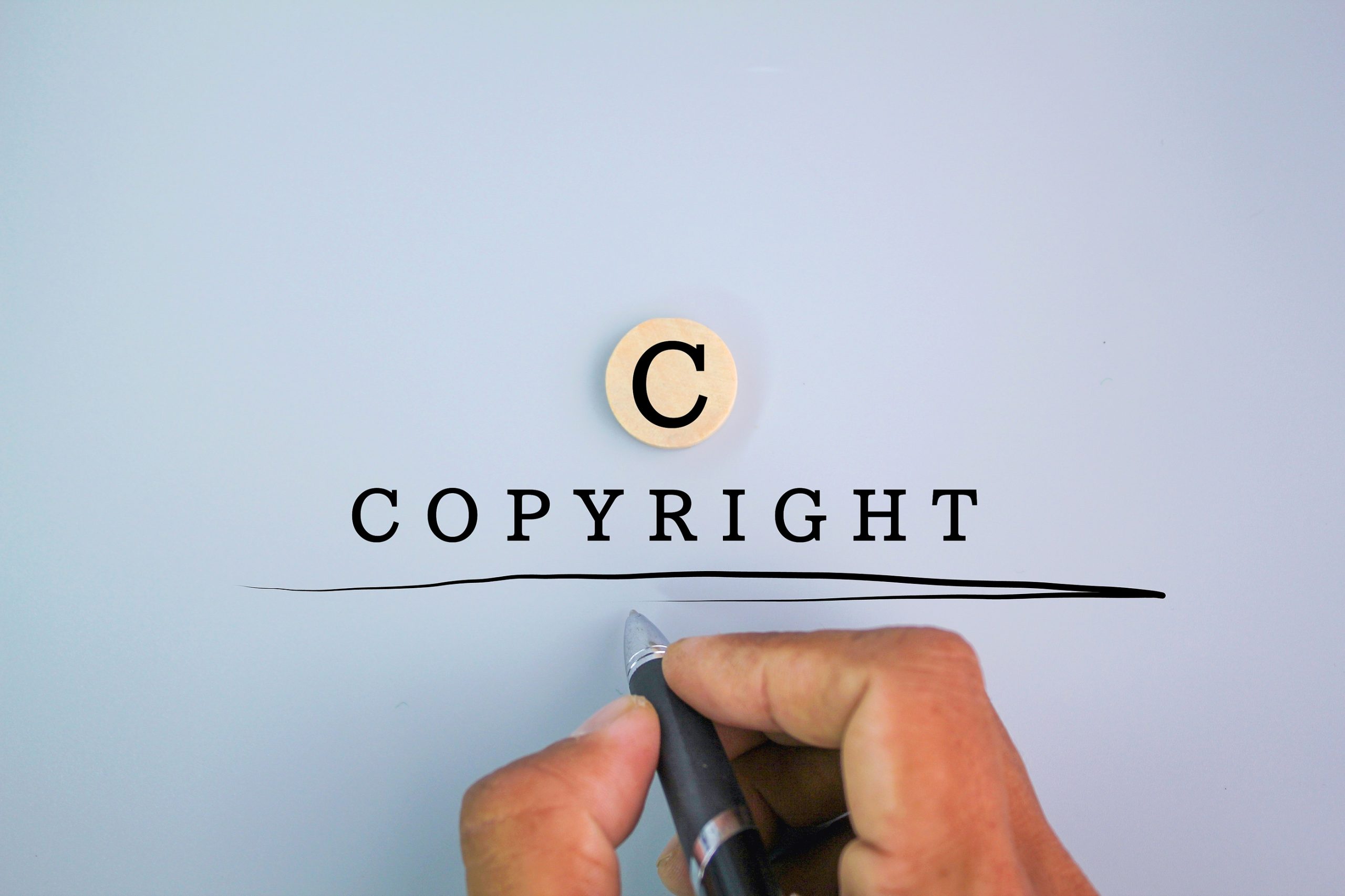 Hand holding a pen and the word copyright with the letter c above.