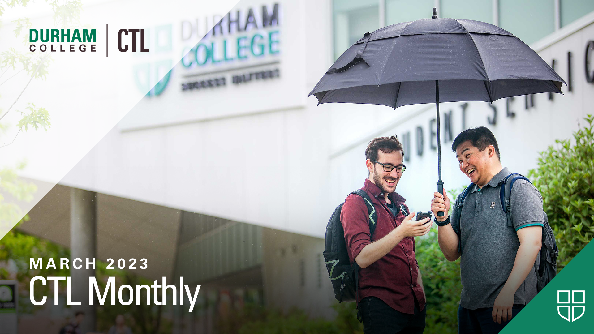 Students standing outside, under an umbrella, looking at a mobile device.