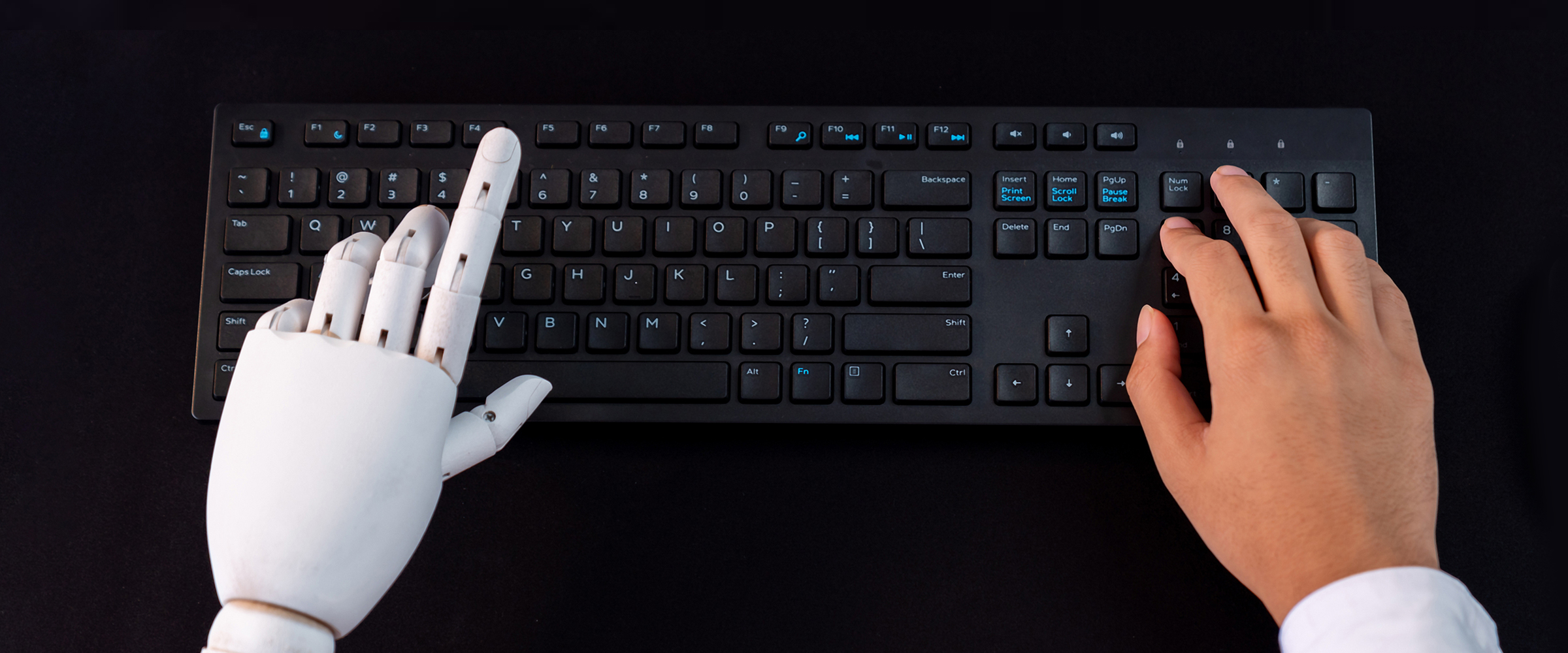 Overhead view of black keyboard with robotic left hand and human right hand