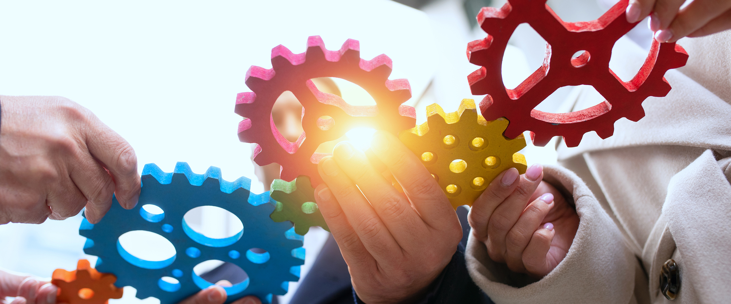Close up of multi-coloured gears being held together by individuals.