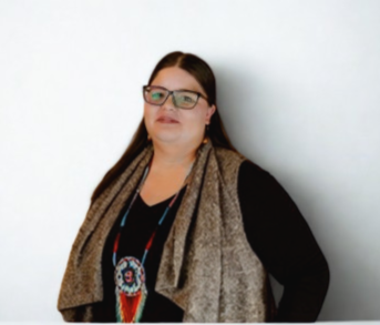 Cassie Hill - A woman with long brown hair and red glasses. Wearing a black long-sleeved shirt with a brown vest and beaded necklace.