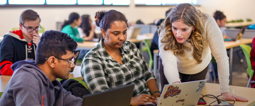 Faculty member supporting two students in the classroom.