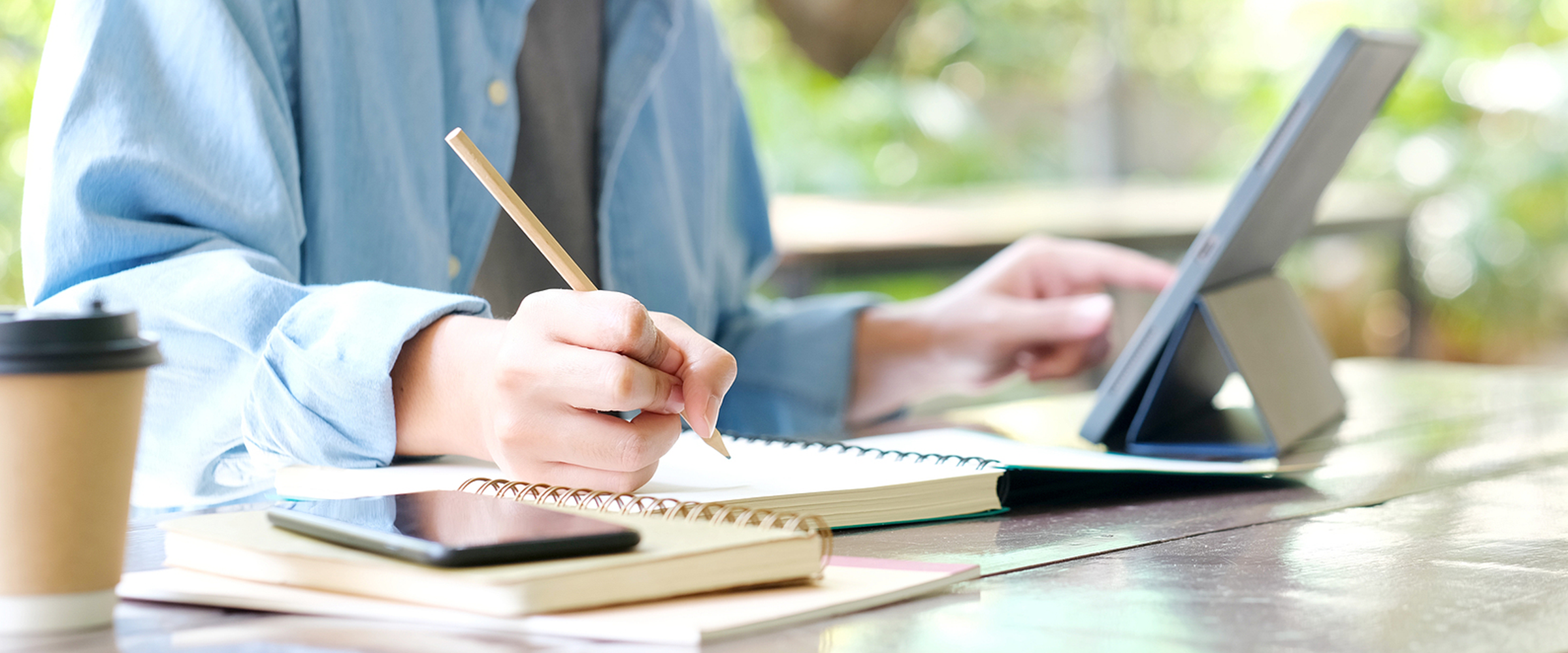 Student handwriting on a notebook while using a digital tablet. 