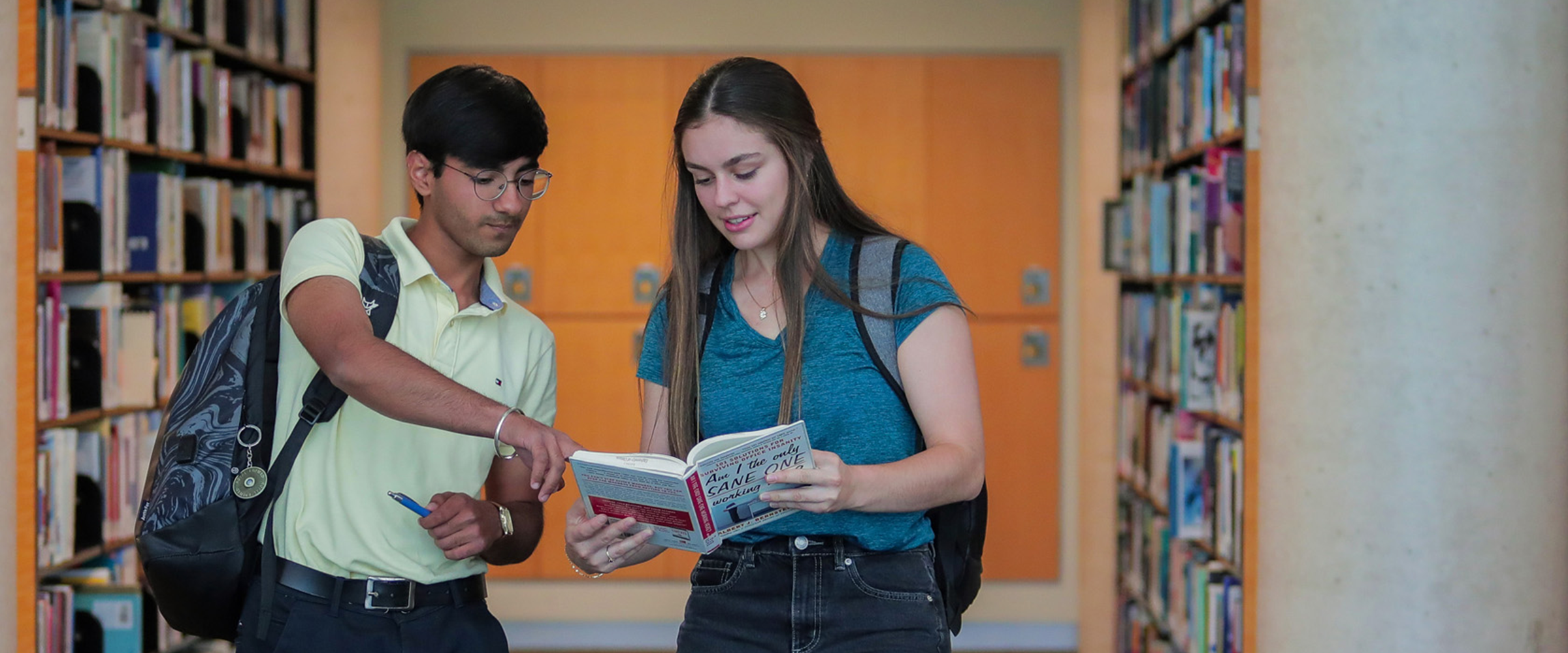 Two students looking at a book in the DC library.