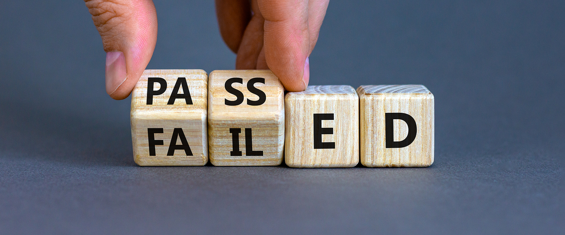 a hand turning wooden cubes, changing the word 'failed' to 'passed'