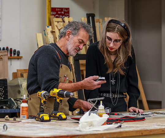 DC faculty member looking at settings on a tool in fabrication class.
