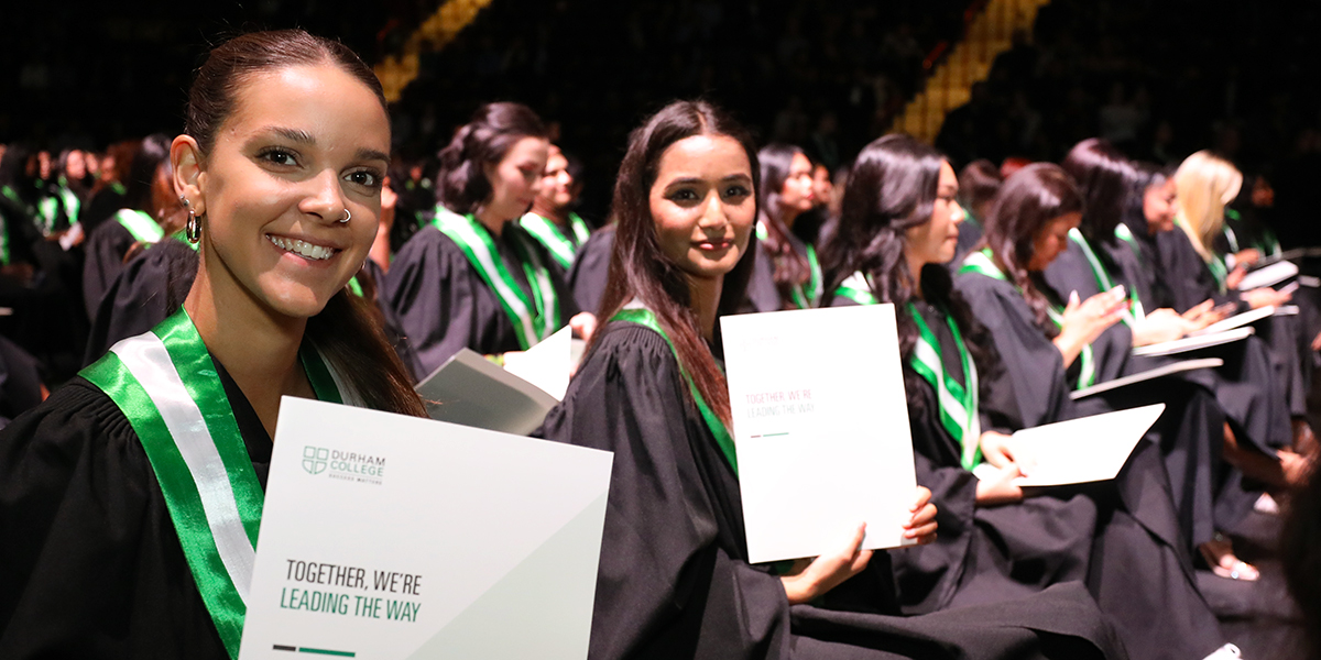 Seated graduates at convocation smile while holding their credentials.