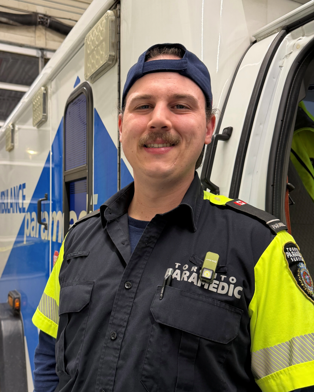Photo of Alex Chipman in paramedic uniform standing in front of an ambulance.