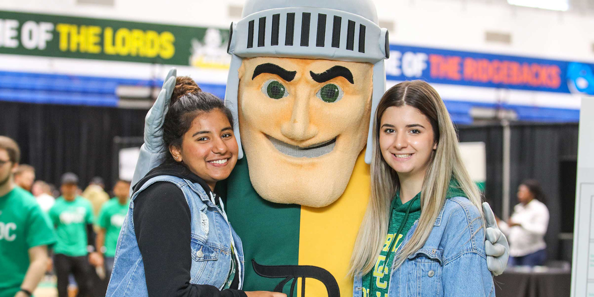 Two students smile and pose with Louie the Lord at Durham College.