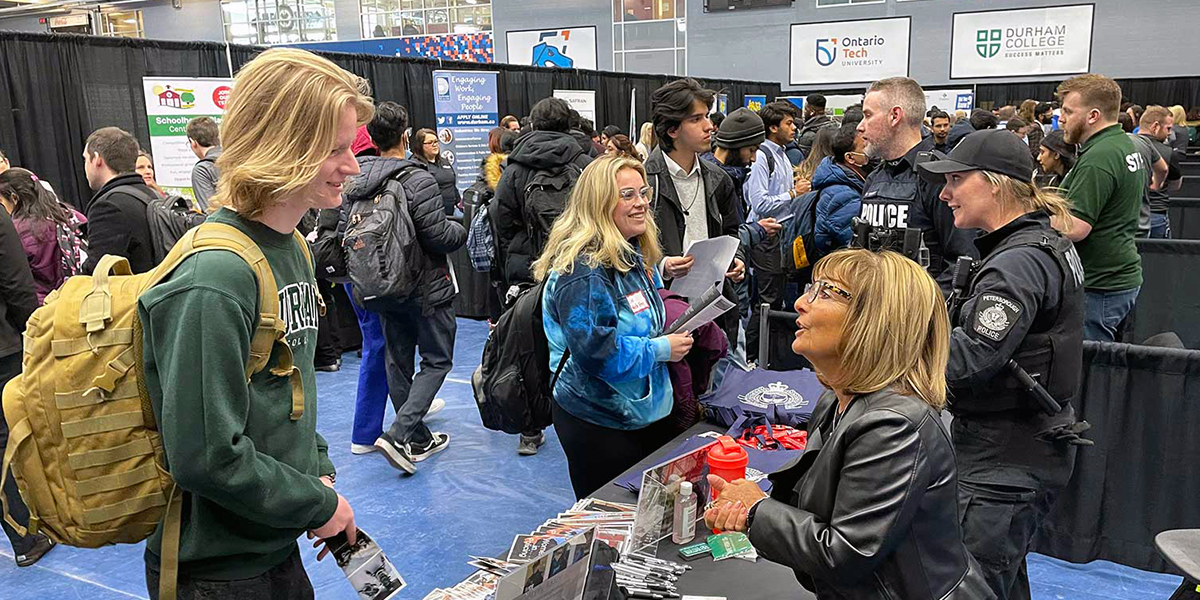 Students speak with an employer sitting at a booth amidst a busy job fair.