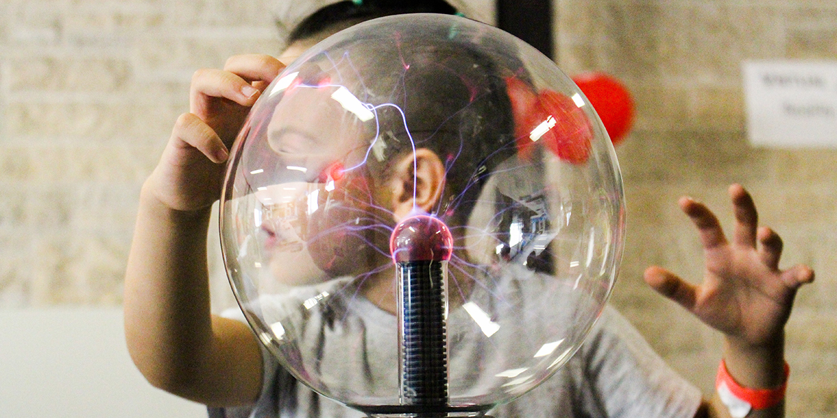 A child moving his hands over a plasma globe