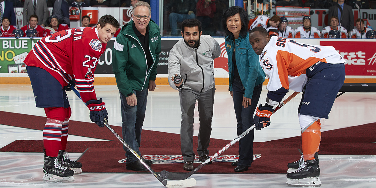 Don Lovisa standing with hockey players at puck drop at alumni night with the generals