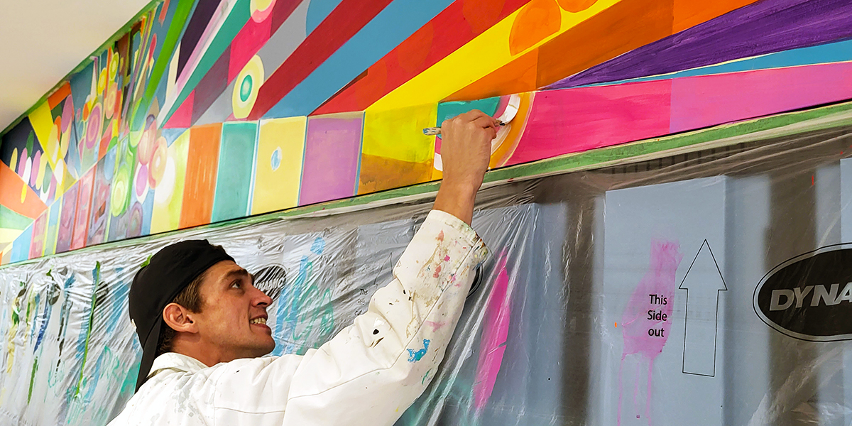 Jordan Dolman smiles while painting a colourful mural.