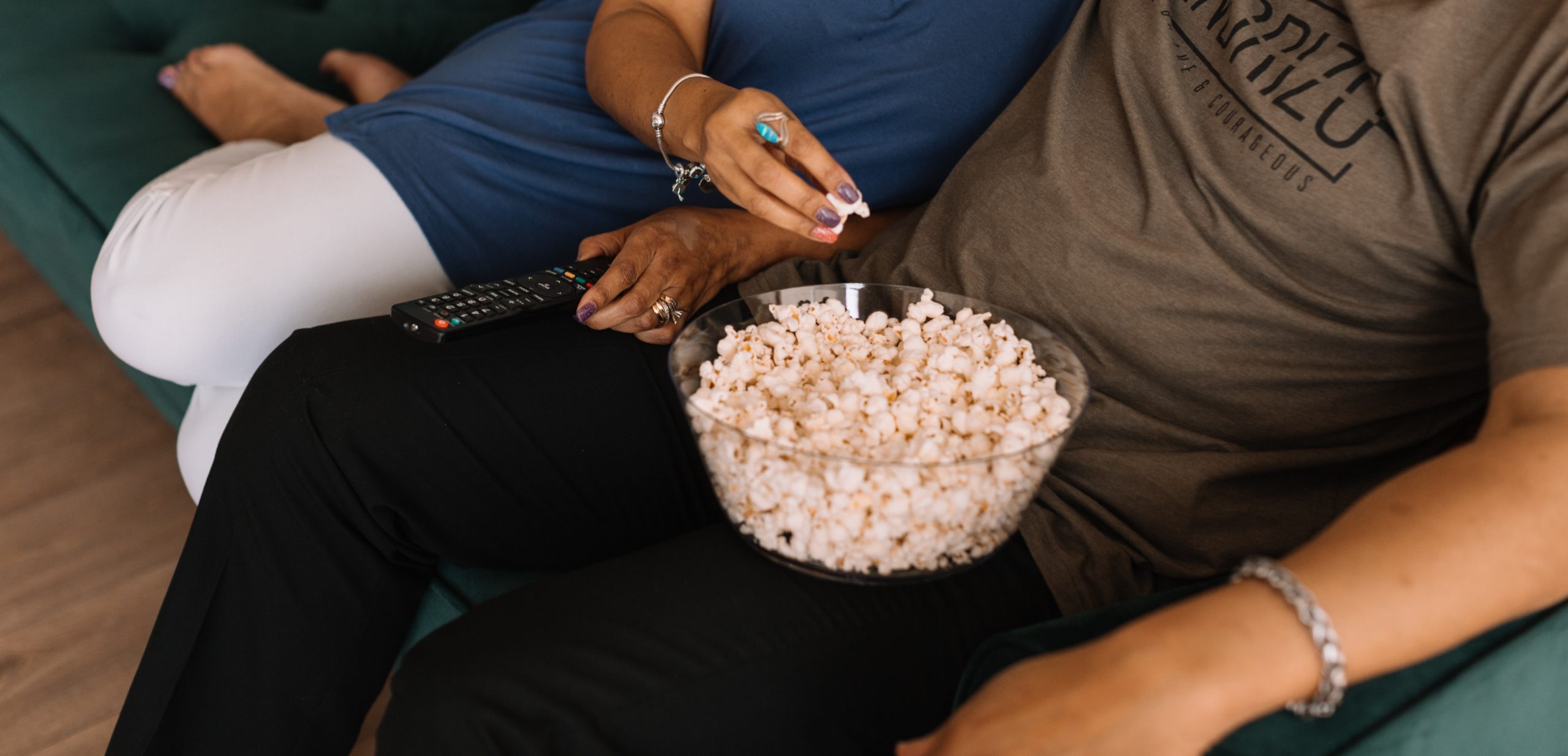 a couple sitting together on the couch watching a movie, with a bowl of popcorn