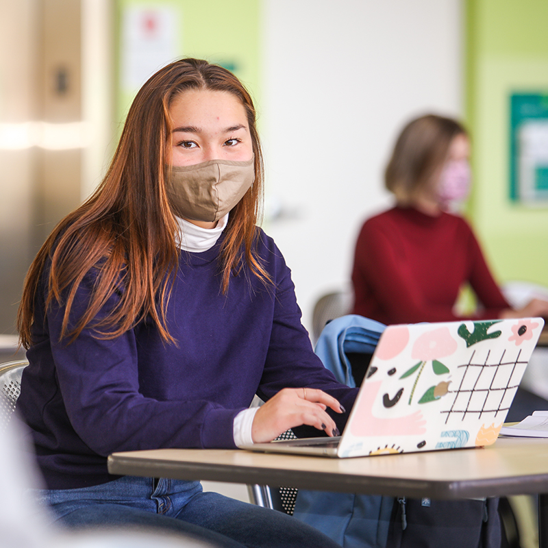 Shot of student in desk with mask and laptop.
