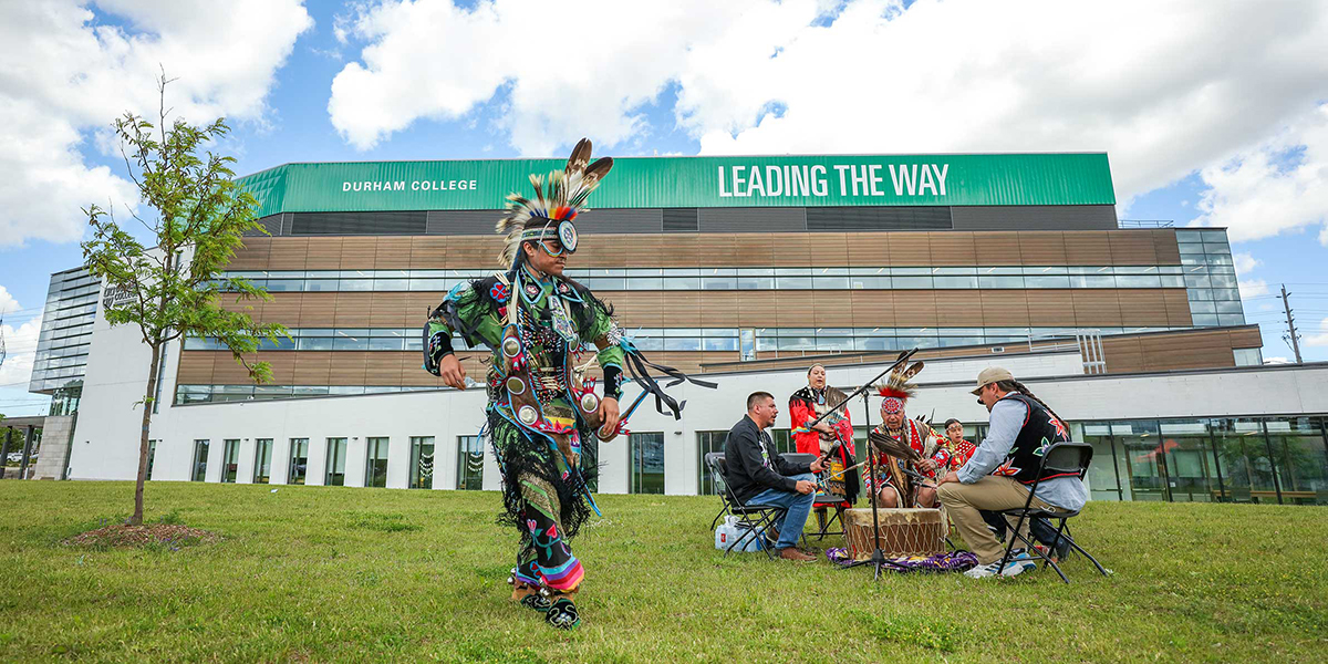 An Indigenous dancer and drum circle perform in front of the CFCE.