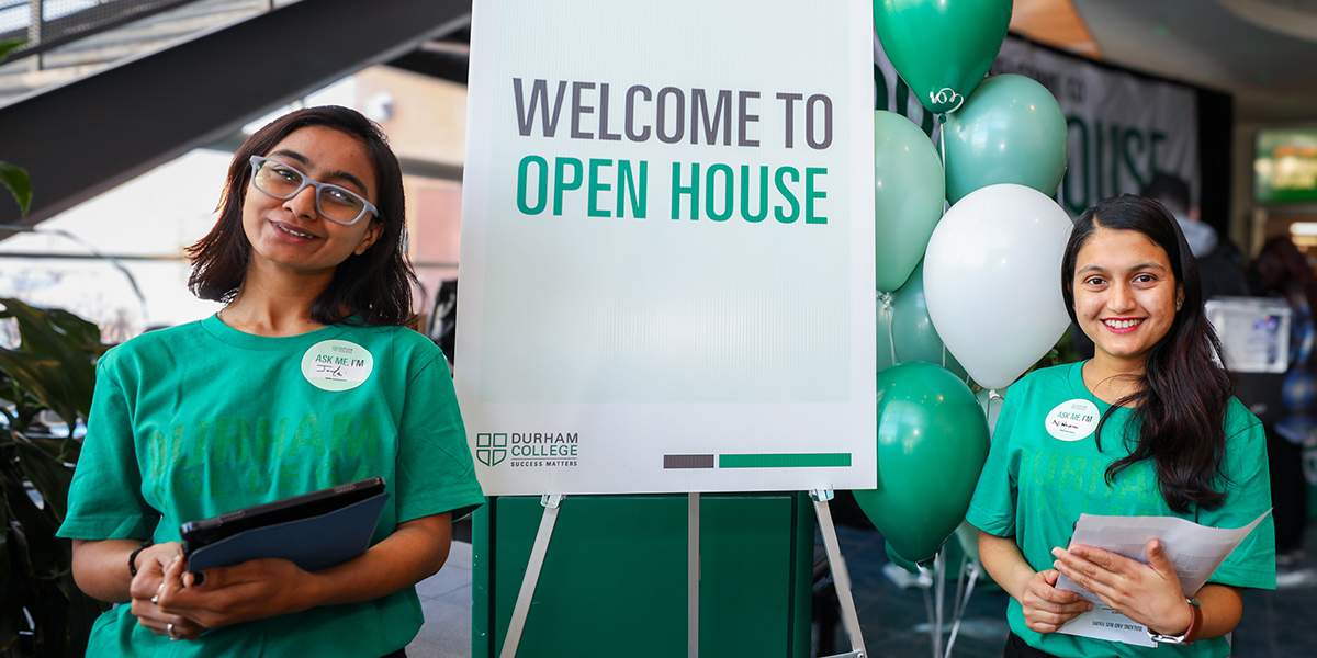 Students in green DC shirts smile in front of a Welcome sign and balloons.