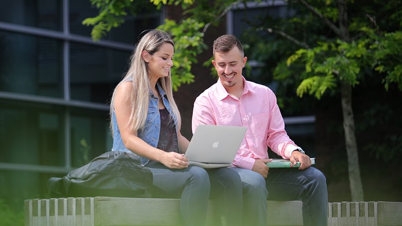 Students sitting at a bench looking at a laptop