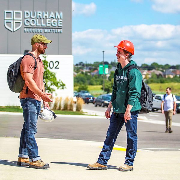 Two trades students talking in front of the Durham College Whitby Campus main building